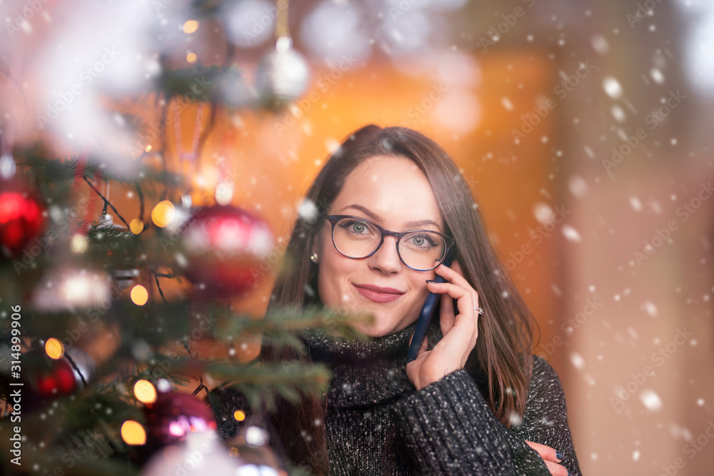 Young woman standing next to the christmas tree and using her mobile phone Young woman standing next to the christmas tree and using her mobile phone