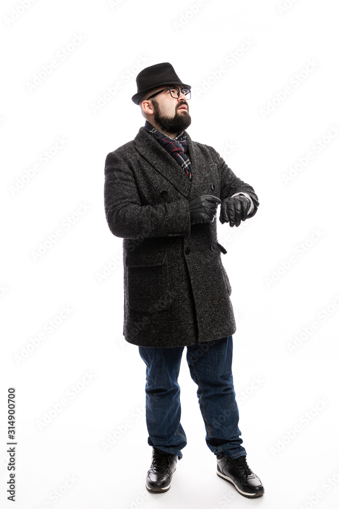 Elegant man with a beard in a coat and hat looks at his watch. Full height. White background. Vertical. Elegant man with a beard in a coat and hat looks at his watch. Full height. White background. Vertical.