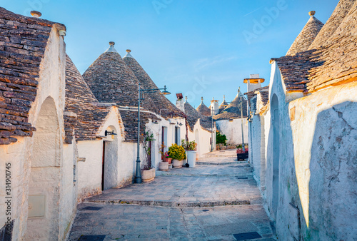 Calm morning view of strret with trullo (trulli) - traditional Apulian dry stone hut with a conical roof. Sunny spring cityscape of Alberobello town, province of Bari, Apulia region, Italy, Europe.