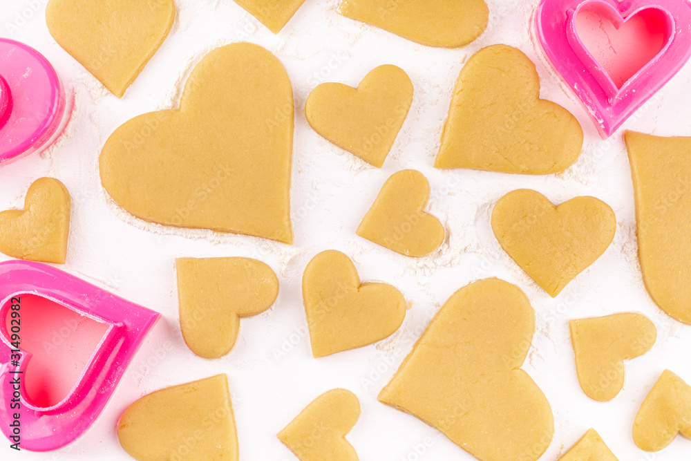 Obraz premium A Lot of Raw Homemade Heart Shaped Cookies with Pink Cookie Cutter and Flour on the White Table. Concept of Happy Valentines Day and Birthday. Top View