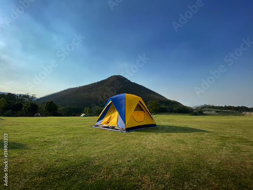 Tourist tent in forest camp among meadow and mountain background.