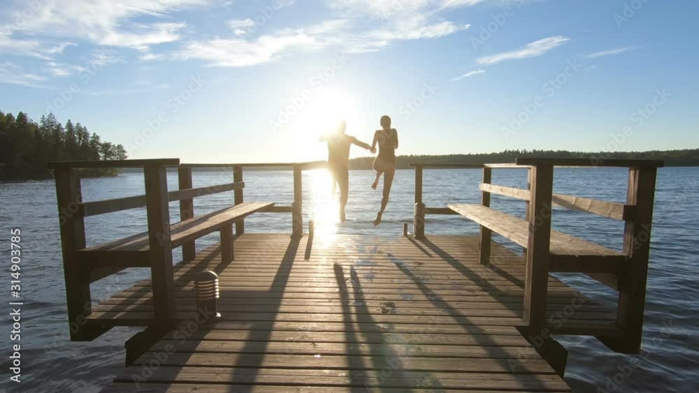 couple running on a wooden pier and jumping into the lake after the sauna in summer white night in Finland.