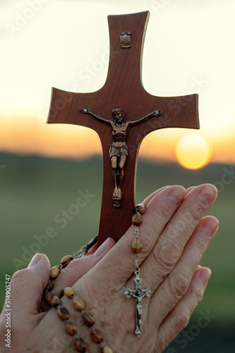 Woman praying outdoor with a crucifix at sunset
