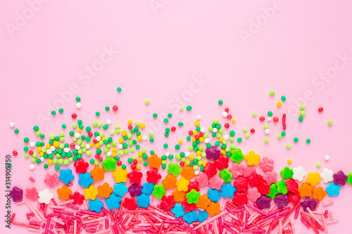 Colorful confectionery topping on a plain pink background with copy space for text  birthday bright background. Festive background with colored sweets.