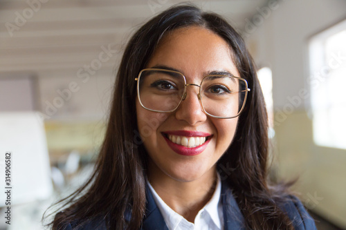 Beautiful young businesswoman smiling at camera. Portrait of attractive young businesswoman in eyeglasses smiling at camera in office. Business concept