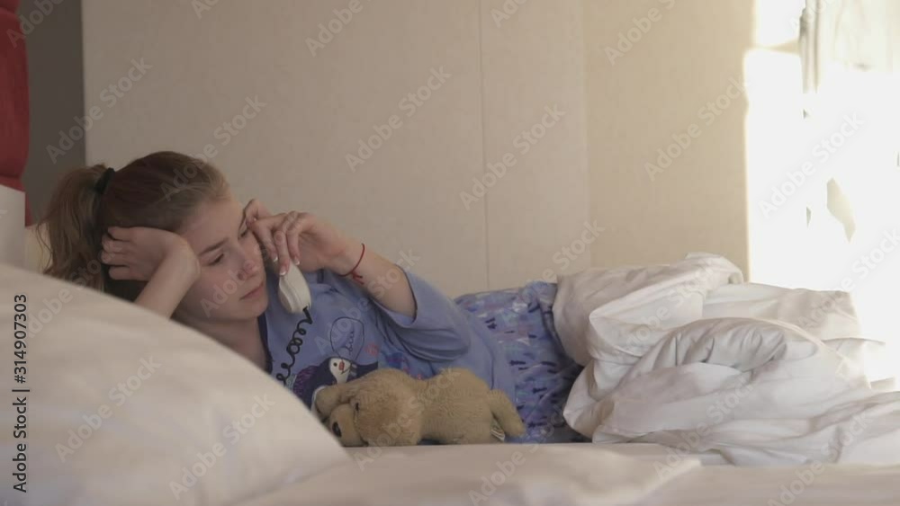 Teenager girl talking on the phone while lying in bed in the hotel Teenager girl talking on the phone while lying in bed in the hotel