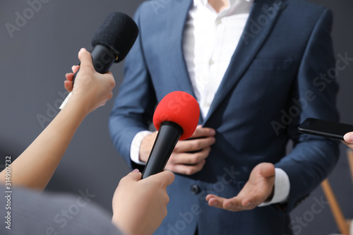 Professional journalists interviewing businessman on grey background, closeup