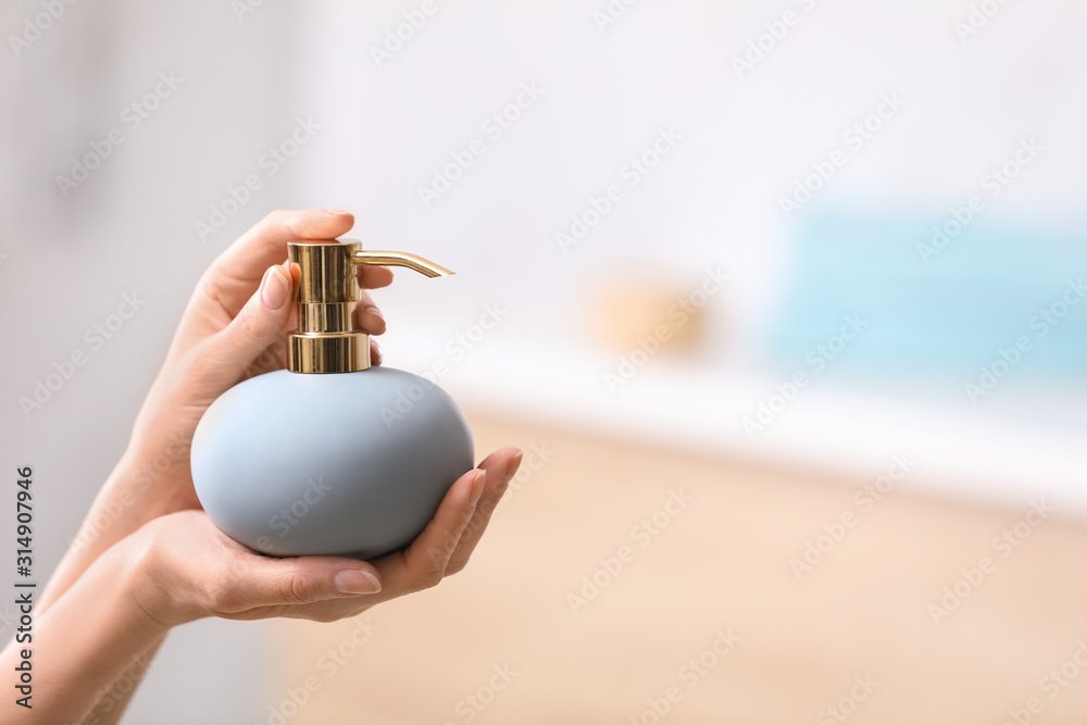 Woman holding soap dispenser on blurred background, closeup. Space for text - obrazy, fototapety, plakaty 