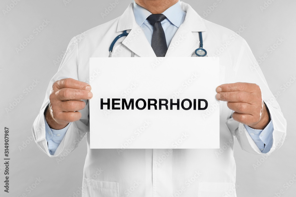 Doctor holding sign with word HEMORRHOID on light grey background, closeup Doctor holding sign with word HEMORRHOID on light grey background, closeup