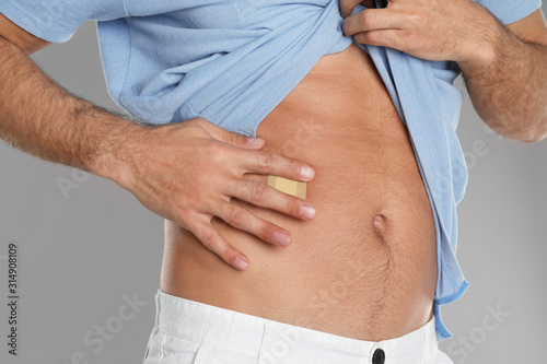 Man with sticking plaster on tummy against light grey background, closeup