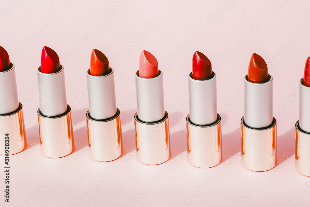 Multi-colored lipsticks stand in a row on a pink background. The concept of different, collections and beauty. Red, pink and burgundy lipsticks Multi-colored lipsticks stand in a row on a pink background. The concept of different, collections and beauty. Red, pink and burgundy lipsticks