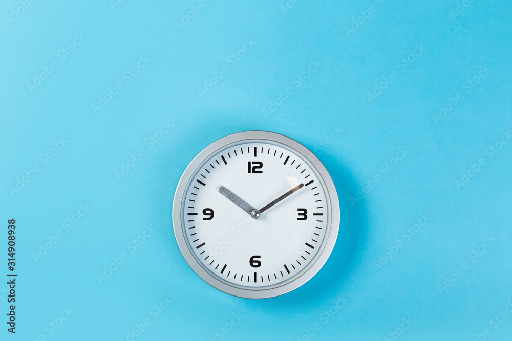 White wall clock with a yellow used hanging on the wall. Minimalist image of a wall clock on a blue background with copy space White wall clock with a yellow used hanging on the wall. Minimalist image of a wall clock on a blue background with copy space