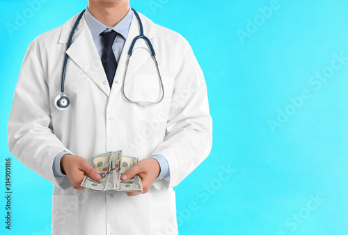 Doctor with bribe on light blue background, closeup. Corruption in medicine photo
