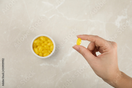 Woman holding tasty lemon drop above light table, top view