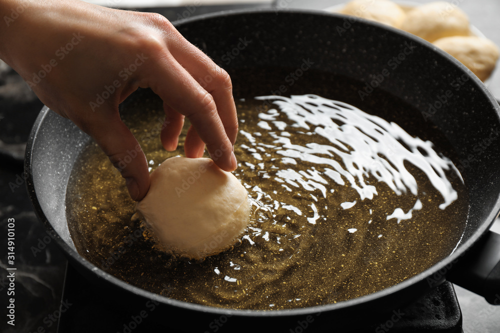 Fototapeta premium Woman cooking delicious donut in hot oil, closeup