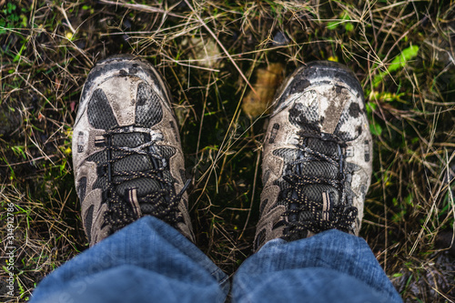 A pair of males walking shoes covering in mud stood on some grass shot from above looking directly down