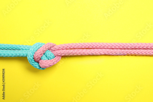 Colorful ropes tied together on yellow background, top view. Unity concept