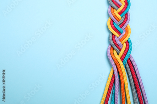 Top view of braided colorful ropes on light blue background, space for text. Unity concept