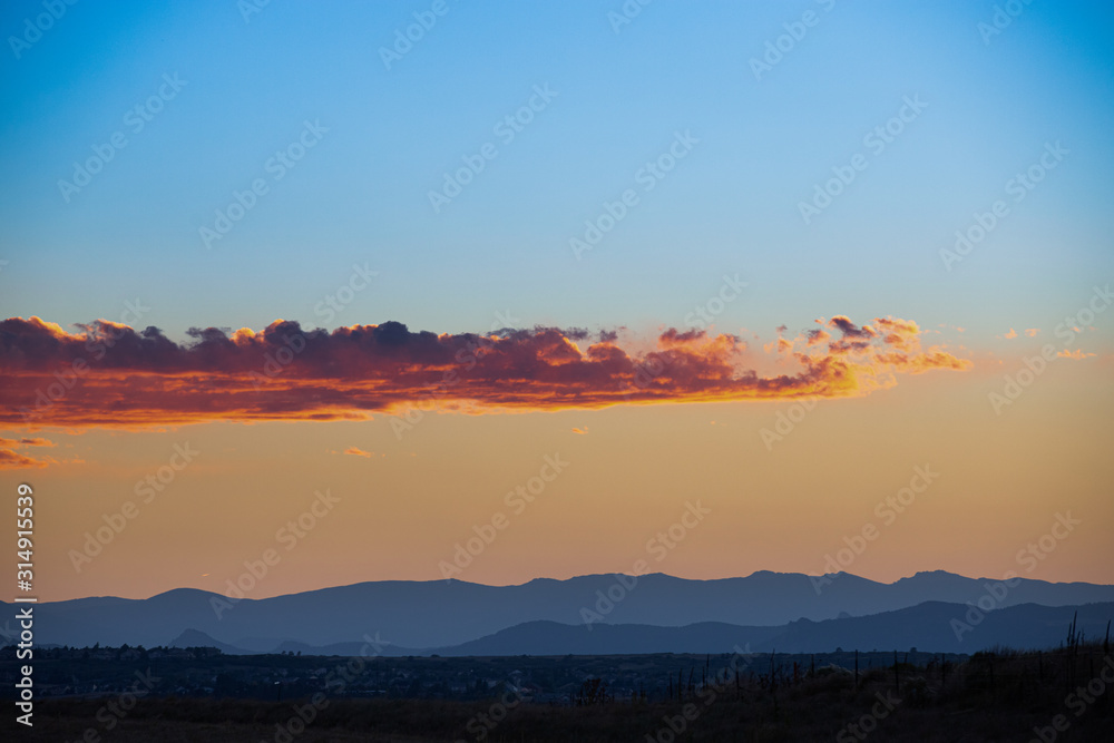 Beautiful gold, orange and blue clouds on sky in twilight during sunset. Shadow Mountains on background 