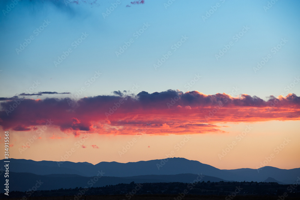 Beautiful gold, orange and blue clouds on sky in twilight during sunset. Shadow Mountains on background 