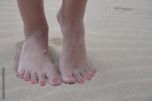 Women's feet on the beach near the sea. The girl took a picture of his feet on the background of sand by the ocean, copy space.
