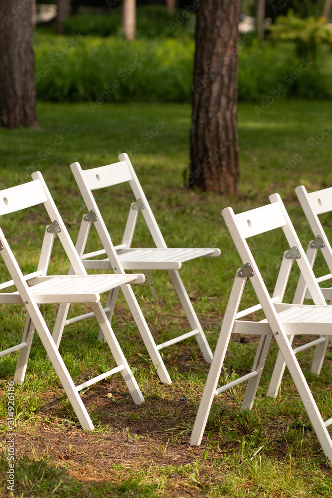 A beautiful place for a wedding ceremony in a clearing in the forest. Many white wooden chairs standing in a row. Luxury wedding ceremony in the open air.