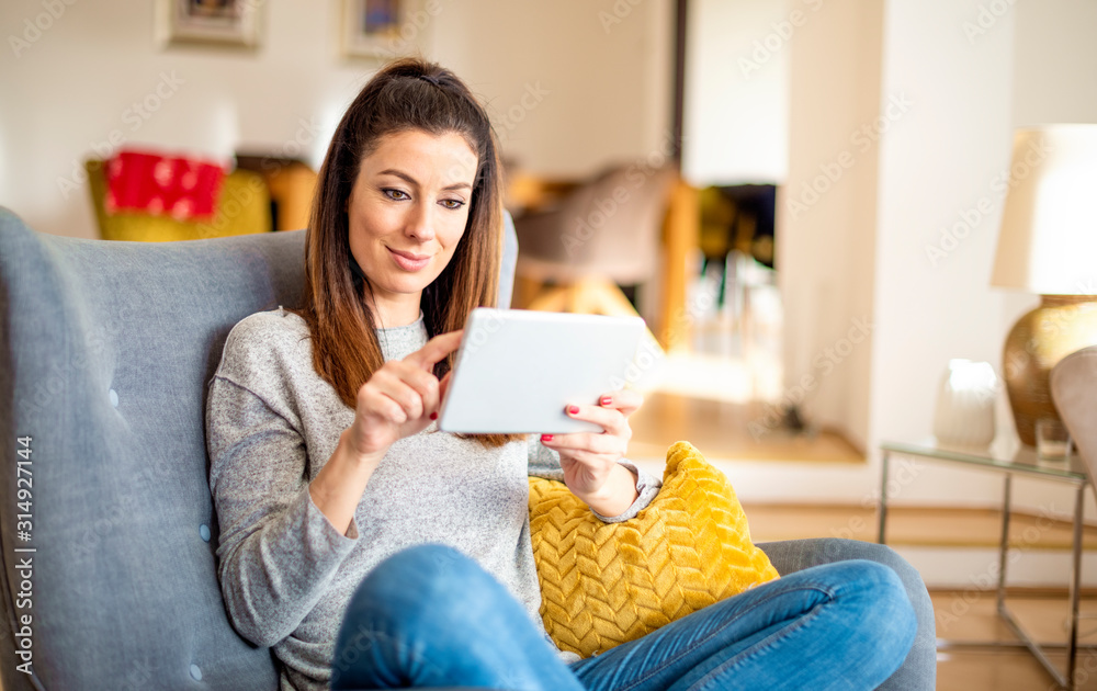 Happy woman using digital tablet while relaxing at home on the sofa