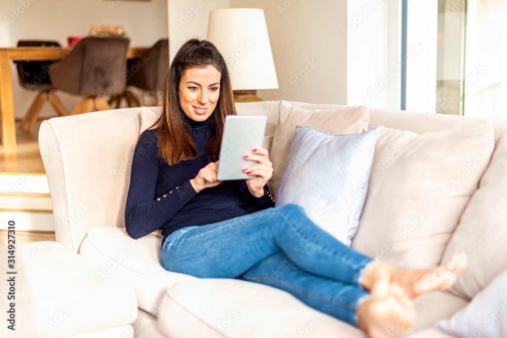 Happy woman using digital tablet while relaxing at home on the sofa Happy woman using digital tablet while relaxing at home on the sofa