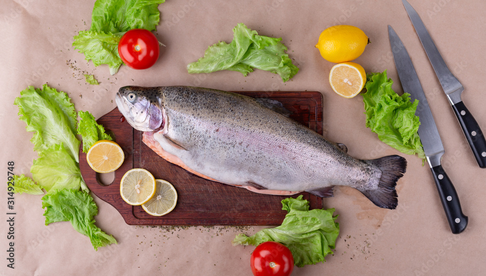 Raw fresh unprepared salmon fish on a wooden board with ingredients for cooking. Lemon, lettuce, tomatoes. Mediterranean cuisine, top view. Raw fresh unprepared salmon fish on a wooden board with ingredients for cooking. Lemon, lettuce, tomatoes. Mediterranean cuisine, top view.