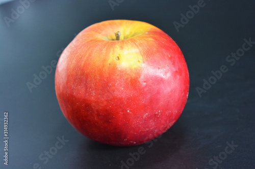 Juicy bright red yellow apple located on a black plastic background.