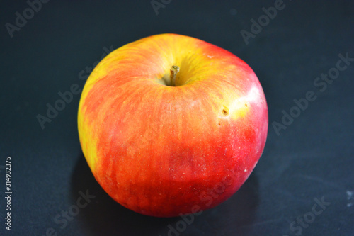 Juicy bright red yellow apple located on a black plastic background.