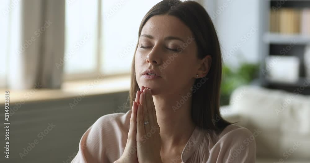 Сhristian young woman saying prayer with eyes closed at home Сhristian young woman saying prayer with eyes closed at home
