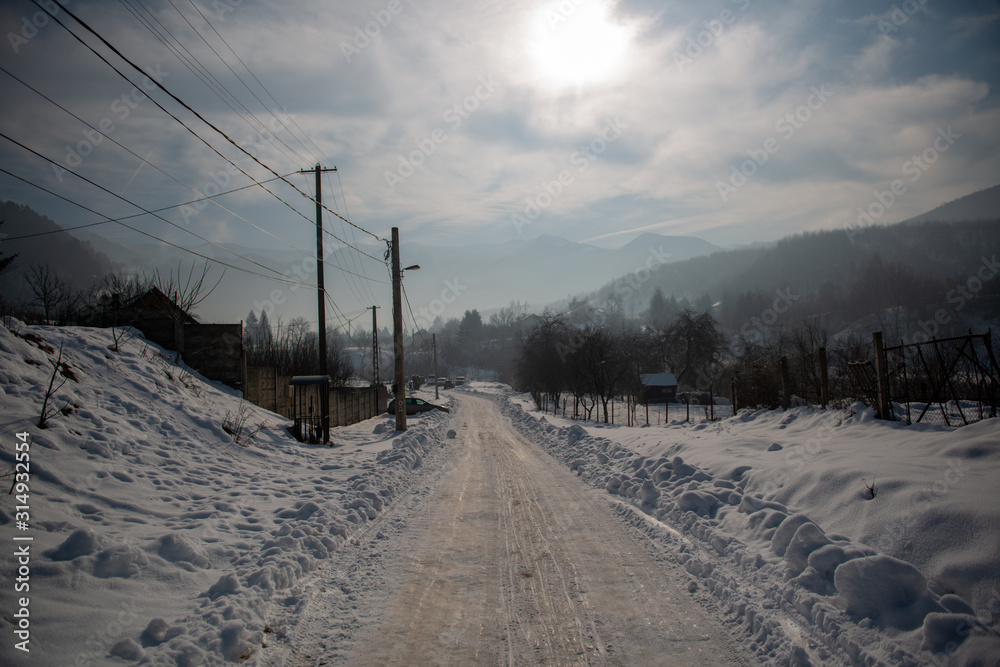 A hazy afternoon in winter times with the sun shining on a snowy dirt road with some telegraph poles and snow walls left and right