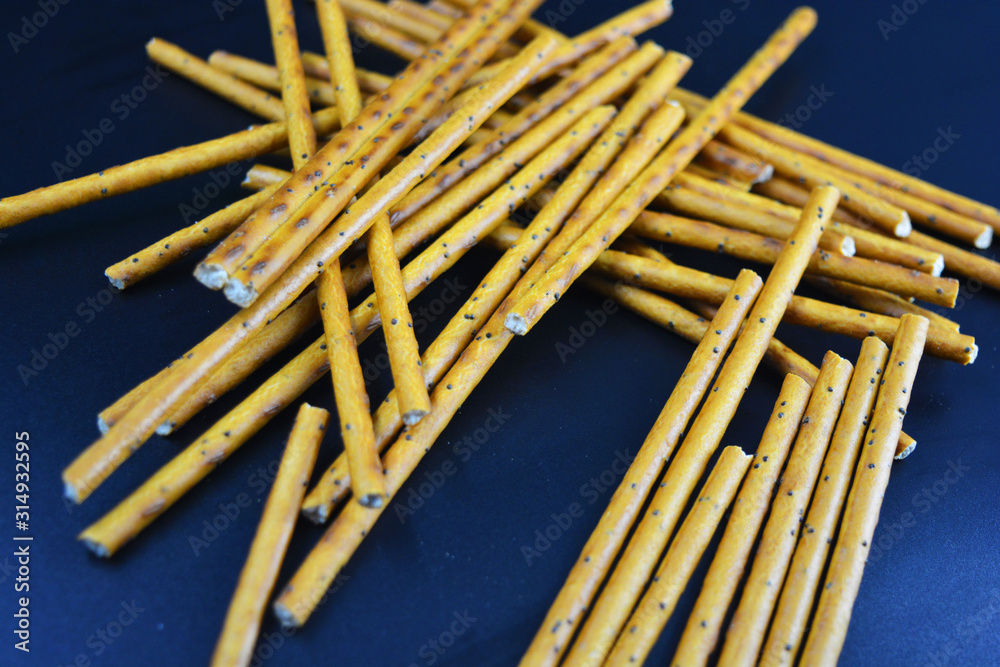 Tasty and sweet straws with poppy seeds made of flour, sneking scattered on a black plastic background. Tasty and sweet straws with poppy seeds made of flour, sneking scattered on a black plastic background.