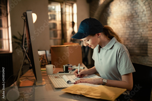 Young female courier filling paperwork in the office.