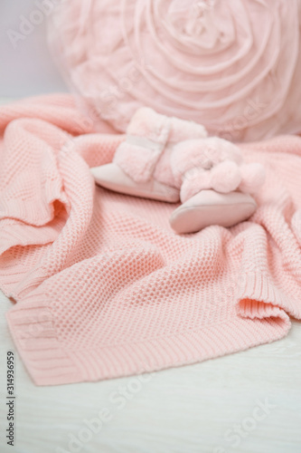 Rose knitted plaid . Pink fluffy baby boots lies atop. Close-up. 