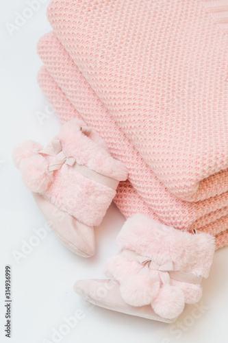 Folded knitted pink plaids. Next to them are fluffy pink baby boots. © Zoja