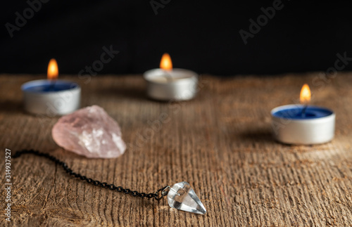 Pendulum on a chain with a natural crystal on a background of wood texture with burning candles.