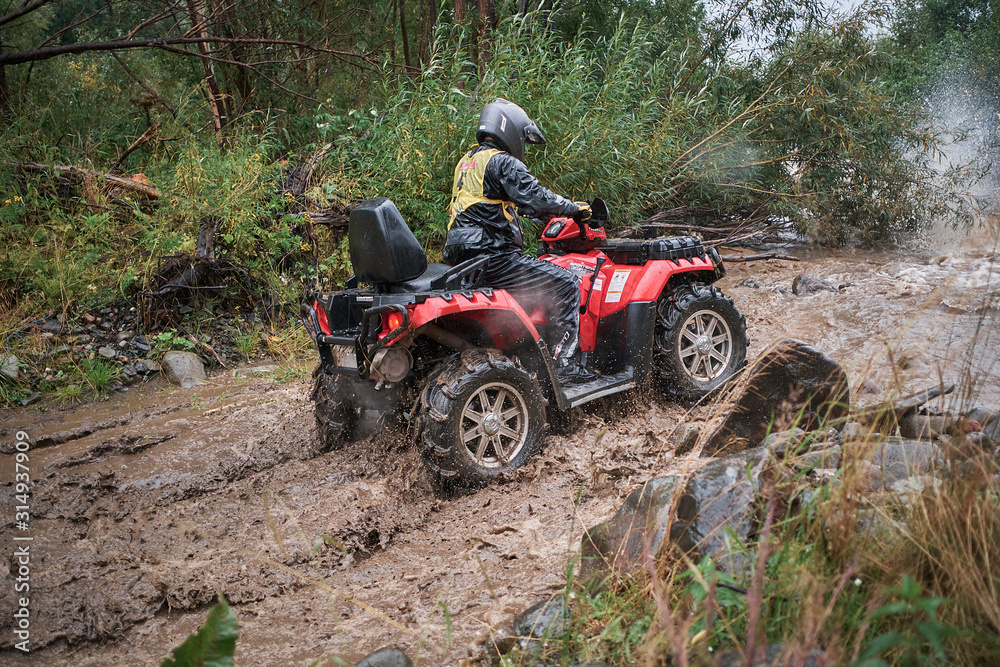 Quad rider jumping on a muddy forest trail.