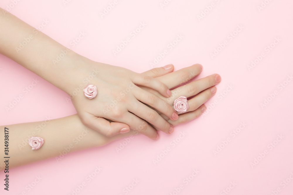 The woman hands hold rose flowers on a pink background. A thin wrist and natural manicure. Cosmetics for a sensitive skin care. Natural petal cosmetics, anti-wrinkle hand care. The woman hands hold rose flowers on a pink background. A thin wrist and natural manicure. Cosmetics for a sensitive skin care. Natural petal cosmetics, anti-wrinkle hand care.