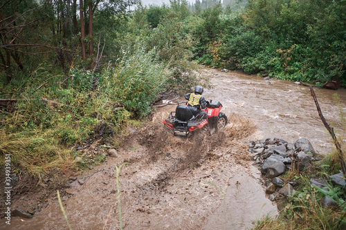 Quad rider jumping on a muddy forest trail.