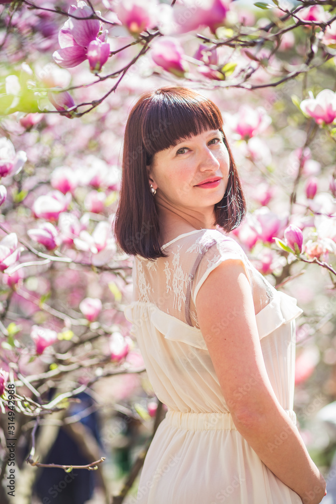 Fototapeta premium Beautiful woman among branches of magnolia in spring in park. Happy Woman on background of pink magnolias in Kiev.