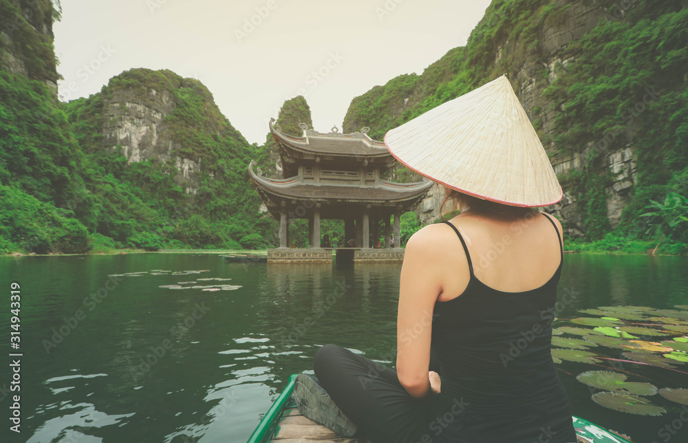 Asian woman sitting on wooden boat during her vacation in Ninh Binh province, Vietnam