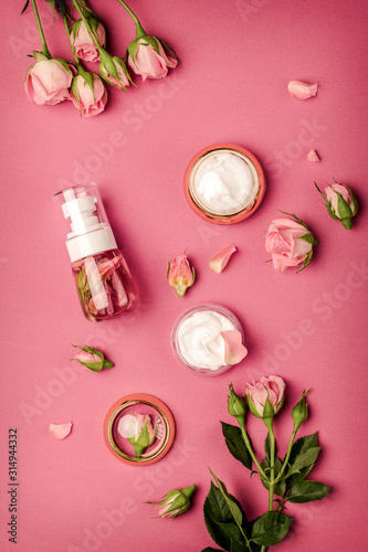 Homemade spa with rose cosmetic set, cream, rose water on pink background top...