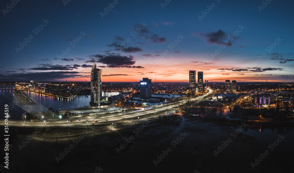 Aerial view over Riga city at night time. Urban landscape with skyscrapers and highway with city lights.