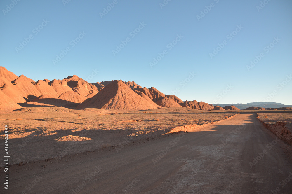 Straight dirt road on the right and mountains on the left at the sunset. Puna labyrinth, Argentina