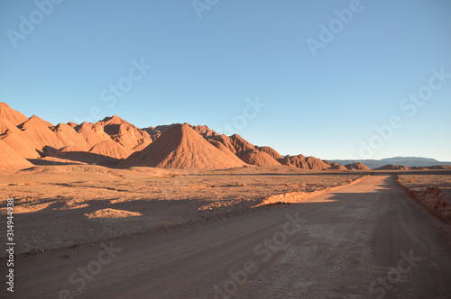 Straight dirt road on the right and mountains on the left at the sunset. Puna labyrinth, Argentina