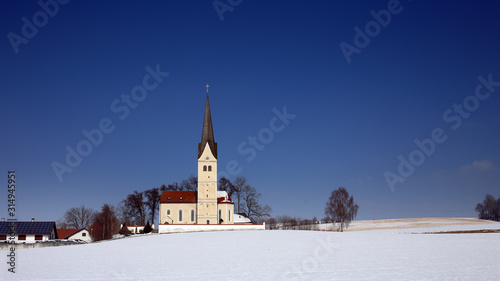 Fraunberg-Riding, Bavaria, Germany. St. Georg church, in winter setting - blue sky, snow fields. 