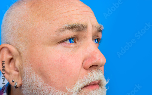 Close up portrait of crying bearded man through hole in blue paper. Copy space for advertising. Discount  sale  season sales. Through paper. Advertising. Close up portrait.