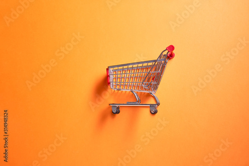 Iron supermarket trolley on empty orange background